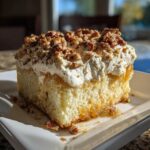 A moist slice of butter pecan praline poke cake topped with whipped cream and chopped pecans.