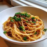Close-up of a white bowl filled with creamy caramelized onion pasta, topped with fresh parsley and red pepper flakes.