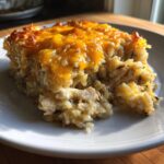 A square serving of creamy chicken and wild rice casserole topped with melted, golden cheddar cheese.
