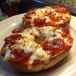 Two freshly baked pizza bagels topped with melted mozzarella cheese, pepperoni slices, and Italian seasoning.