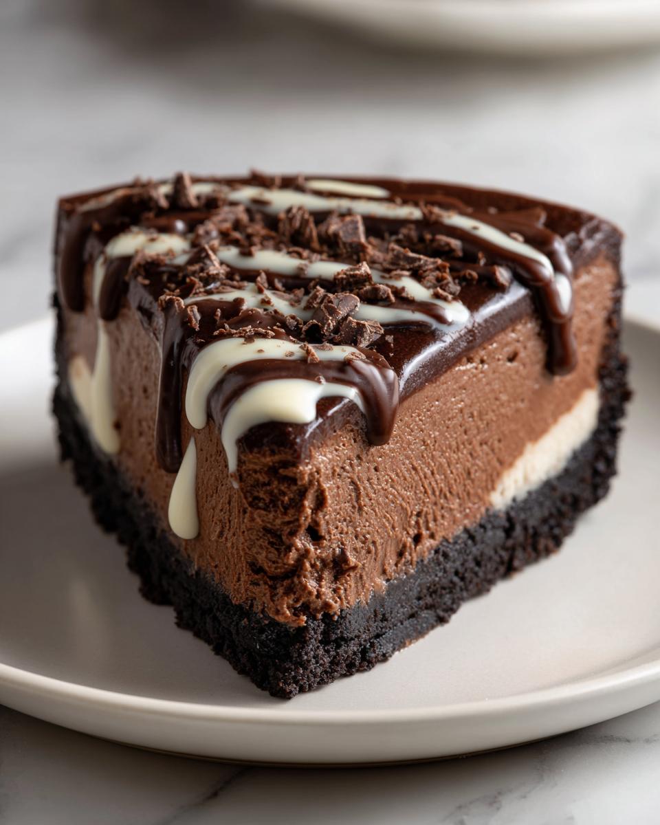A rich slice of chocolate cheesecake with a dark cookie crust, topped with chocolate ganache and white chocolate drizzle.
