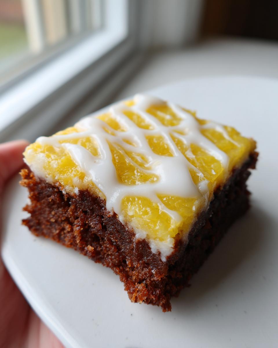 A single square of chocolate lemon brownies featuring a bright yellow layer and white icing drizzle.