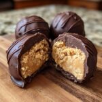 A close-up of chocolate-covered peanut butter balls, one cut in half revealing the creamy peanut butter filling.