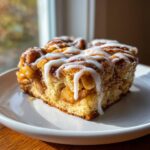 A close-up of a square slice of cinnamon roll apple pie covered in thick white icing.