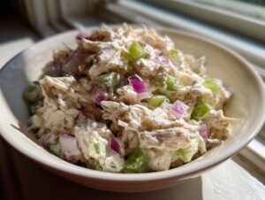 Close-up of creamy cottage cheese chicken salad mixed with diced celery and red onion in a small white bowl.