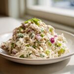 A mound of creamy cottage cheese chicken salad mixed with diced red onion and celery, garnished with green onion.