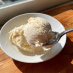 A spoonful of creamy, vanilla-colored cottage cheese ice cream being lifted from a white bowl.