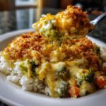 A spoonful of creamy broccoli vegetable casserole with a crispy topping being lifted from a serving on white rice.