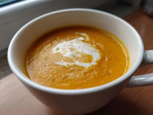 Close-up of creamy, bright orange butternut squash soup topped with a swirl of cream.