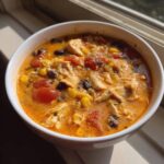 A close-up of a hearty bowl of creamy chicken taco soup with shredded chicken, black beans, corn, and tomatoes.