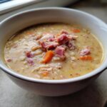 Close-up of a creamy navy bean soup bowl, garnished generously with diced ham and carrots.