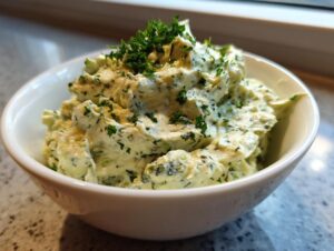 Close-up of a creamy, pale green olive dip served in a white bowl and garnished with chopped fresh parsley.