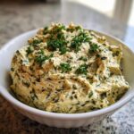 A close-up of a bowl filled with creamy, textured olive dip speckled with dark pieces and topped with fresh chopped parsley.