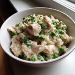 Close-up of creamy one pot chicken and rice mixed with bright green peas and topped with fresh parsley.