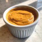 Close-up of thick, orange burger sauce speckled with spices, served in a small white ramekin.