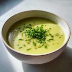 A bowl of creamy, pale green potato leek soup garnished generously with freshly chopped chives.