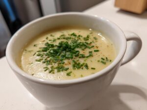 A close-up of creamy potato leek soup topped with fresh chopped chives in a white mug.