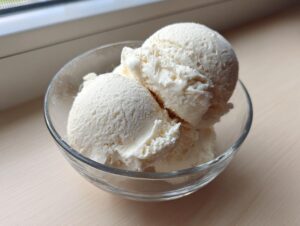 Three scoops of creamy vanilla-colored protein ice cream served in a small clear glass bowl.