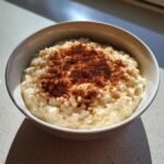 A close-up of creamy rice pudding recipe served in a white bowl, generously dusted with ground cinnamon.