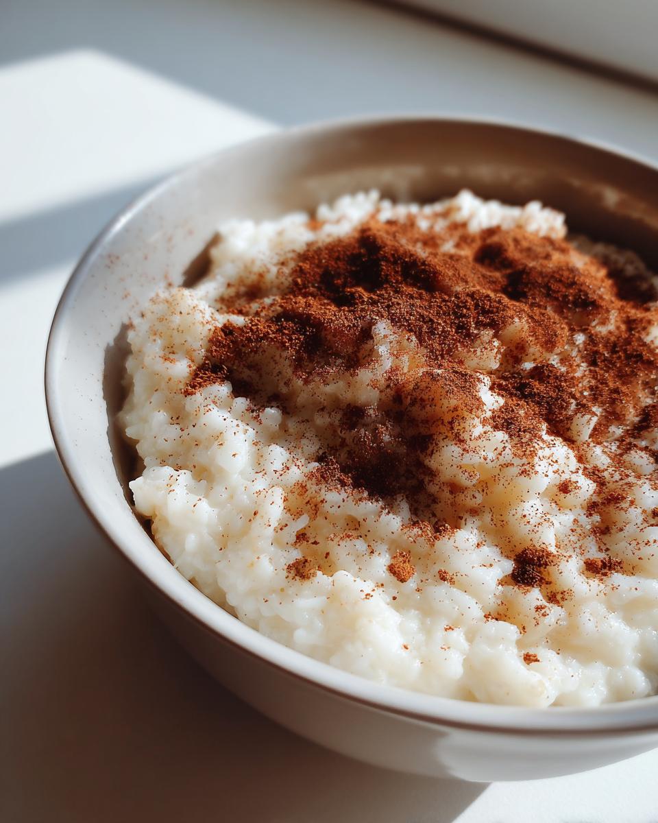 Close-up of creamy rice pudding recipe served in a light bowl, generously dusted with ground cinnamon.