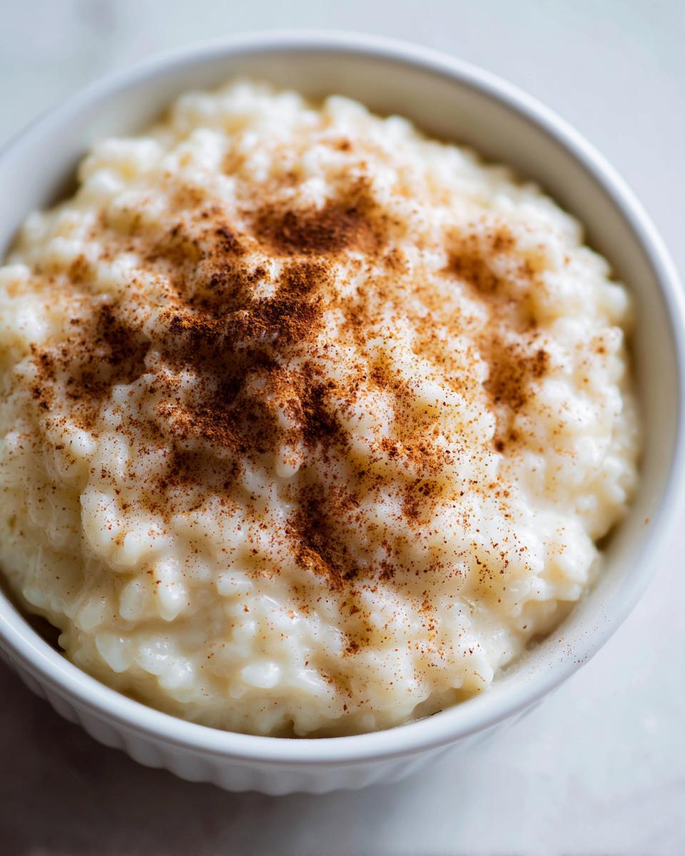 Close-up of creamy rice pudding recipe served in a white bowl, generously dusted with cinnamon.