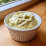 A close-up of creamy, homemade tartar sauce recipe garnished with green herbs, served in a white ramekin.