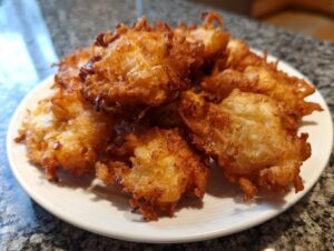 A pile of golden brown, crispy Amish Onion Fritters served on a white plate.