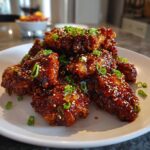 Close-up of crispy Korean fried chicken pieces coated in a dark, glossy sauce and topped with sesame seeds and scallions.