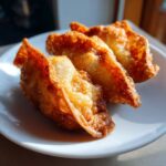 Close-up of three golden brown, crispy fried rice paper dumplings arranged on a white plate.