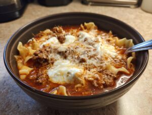 A close-up of a bowl of rich, meaty crockpot lasagna soup topped with dollops of ricotta and shredded mozzarella cheese.