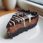 A rich slice of chocolate cheesecake with a dark crust, chocolate ganache, and white chocolate drizzle.