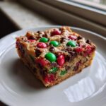 A close-up of a thick, chewy christmas cookie bars square topped with red and green M&Ms.
