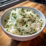A white bowl filled with fluffy cilantro lime rice, garnished generously with chopped green herbs.