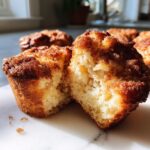 Close-up of a fluffy french toast muffin broken in half, showing the soft interior and cinnamon-sugar topping.