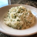 A close-up of fluffy white garlic butter rice topped generously with chopped fresh parsley in a white bowl.
