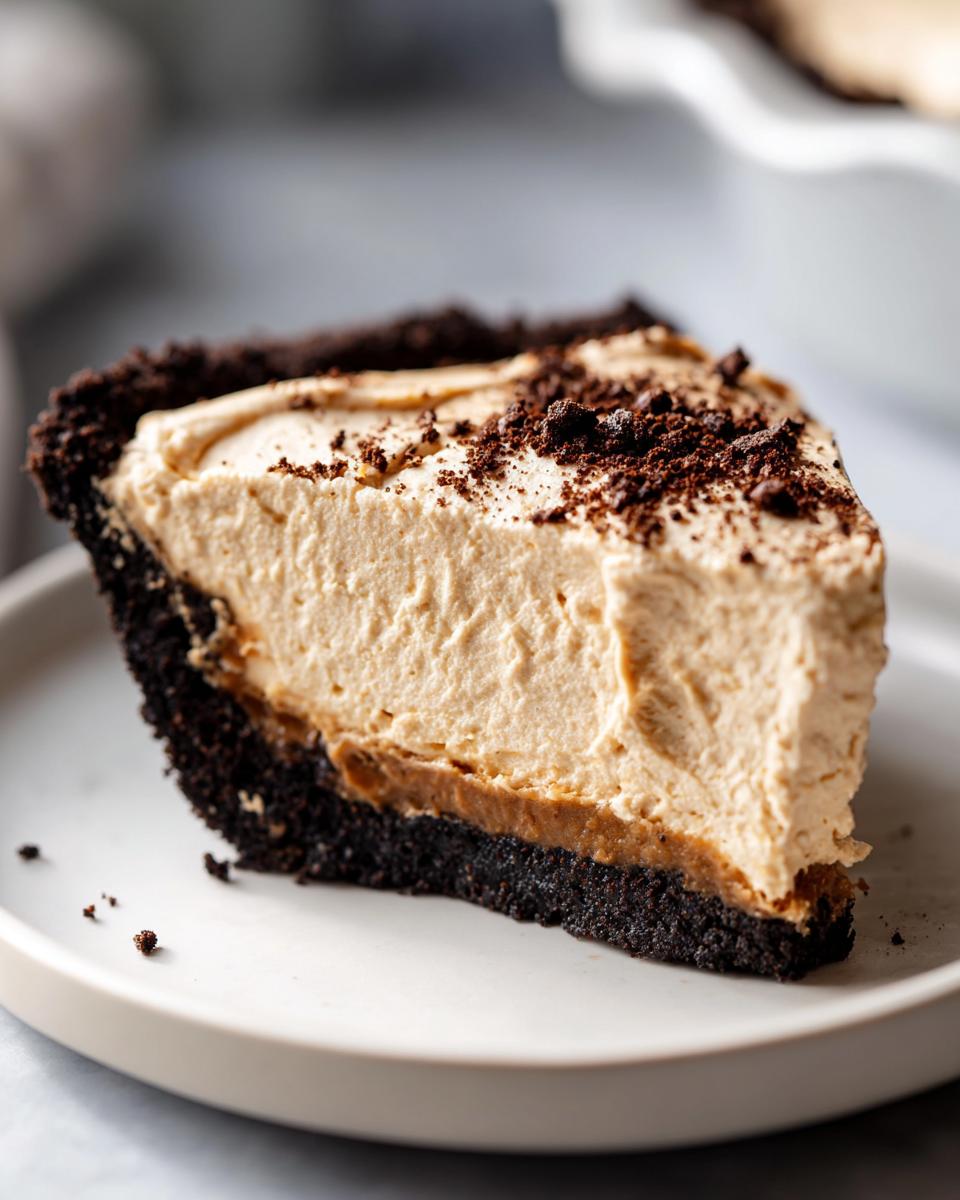 A thick slice of no bake peanut butter pie with a dark chocolate crust, served on a white plate.