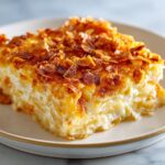 A close-up of a creamy, cheesy slice of funeral potatoes recipe topped with crispy, browned cornflakes.