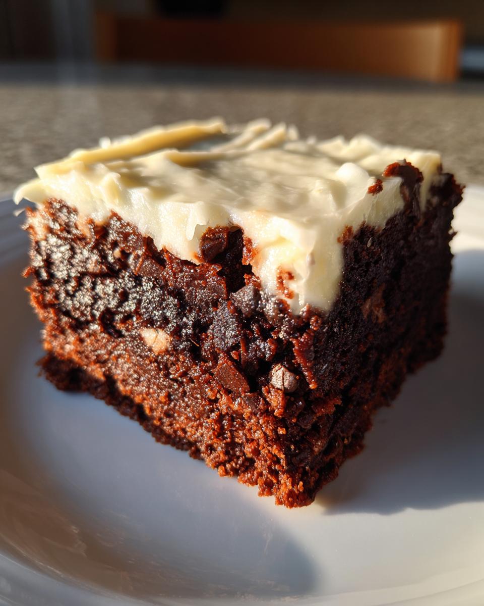 A close-up, sunlit square slice of rich, dark gingerbread brownies topped with thick white cream cheese frosting.