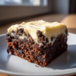A single square of rich, dark gingerbread brownies topped with thick, creamy frosting.