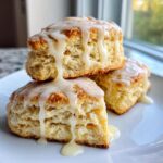 Three flaky lemon scones stacked and drizzled heavily with a thick white glaze.
