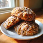 Three soft, glazed persimmon cookies stacked on a white plate near a window.