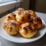 A plate of freshly baked, golden brown pizza bites topped with melted cheese and small dark toppings.