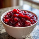 Close-up of glistening, chunky homemade cranberry sauce served in a small white bowl.