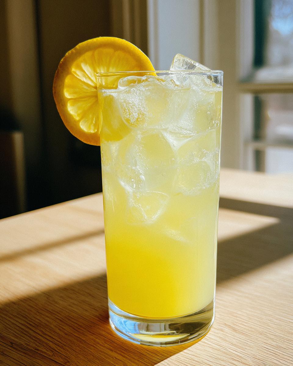 A tall glass filled with ice and bright yellow homemade lemonade, garnished with a fresh orange slice.