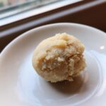 A close-up of a small, textured ball of homemade marzipan recipe paste resting on a white saucer.