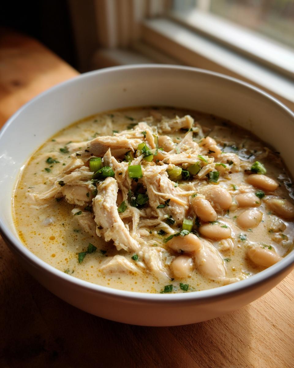 A close-up of a creamy bowl of instant pot white chicken chili topped with shredded chicken, white beans, and green onions.