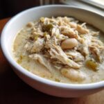 Close-up of a white bowl filled with creamy instant pot white chicken chili featuring shredded chicken and white beans.