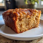Close-up of a moist slice of applesauce cake showing its tender crumb and shiny, caramelized topping.