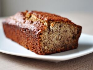 A close-up of a freshly baked, moist banana bread loaf with a dark golden crust, sliced to show the crumb texture.