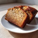 Two thick slices of moist banana bread showing a rich brown crust and soft interior, served on a white plate.